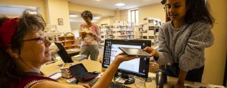 Une bibliothécaire tend une liseuse électronique à une jeune fille.