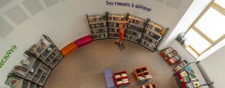 Intérieur d'une bibliothèque vu de haut avec une personne choisissant un livre dans une étagère