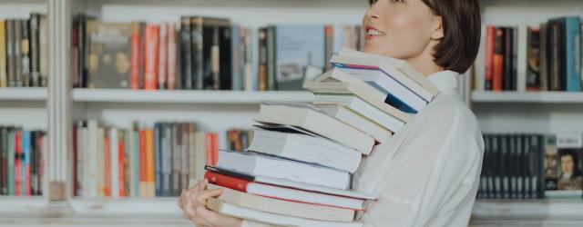 femme portant une pile de livres devant des rayonnages de bibliothèque